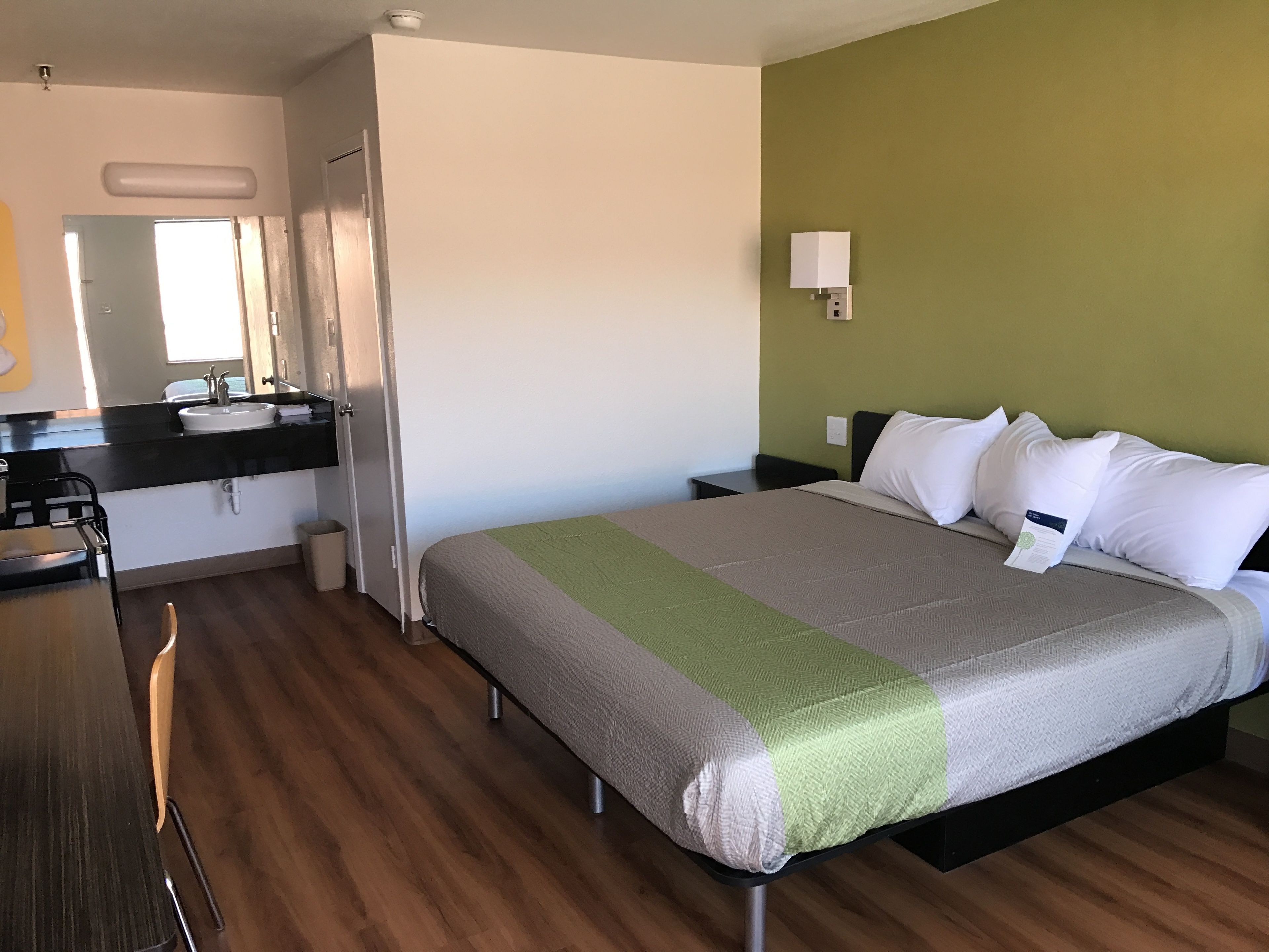 Een hotelkamer met een bed, een bureau, een stoel, een wastafel en een spiegel.