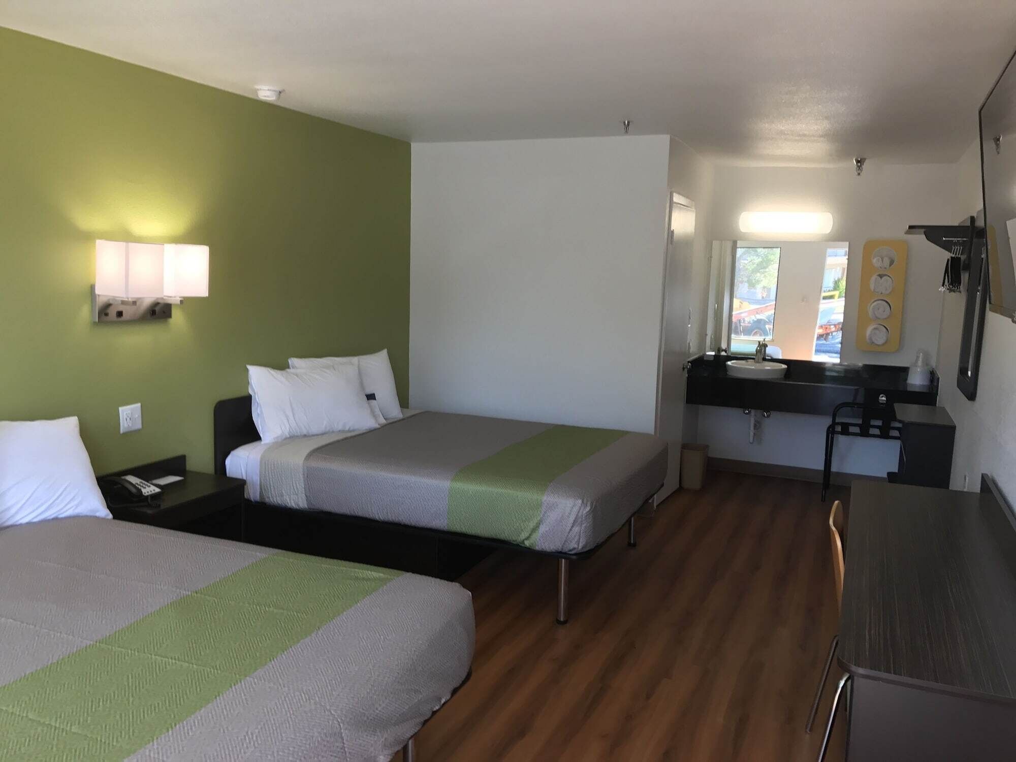 A hotel room with two beds, a small desk, a sink, and a mirror.