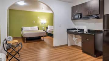 A compact hotel room with a bed, a kitchenette, and a small seating area.