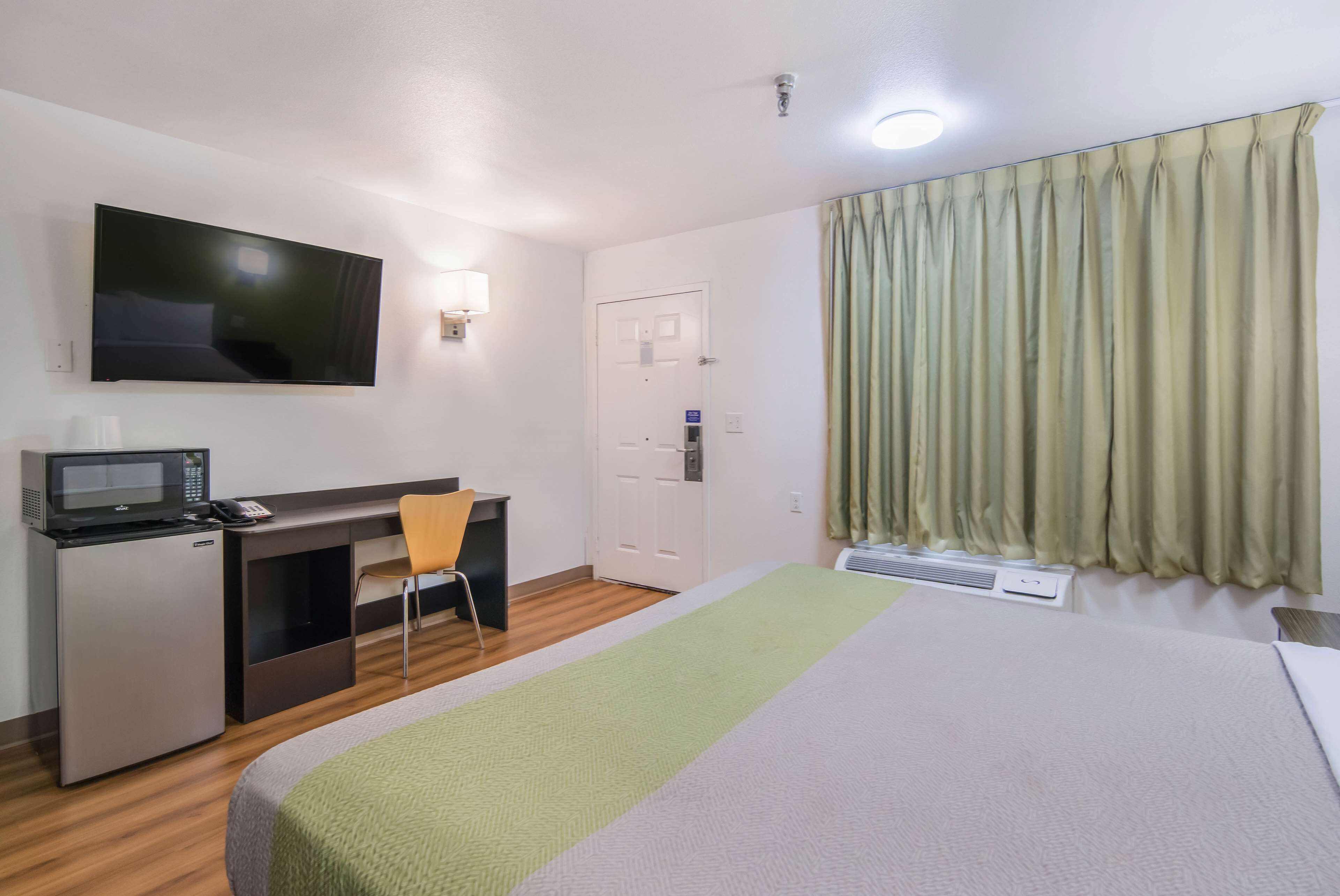 A hotel room with a bed, a desk with a computer, a TV, a microwave, and a chair.