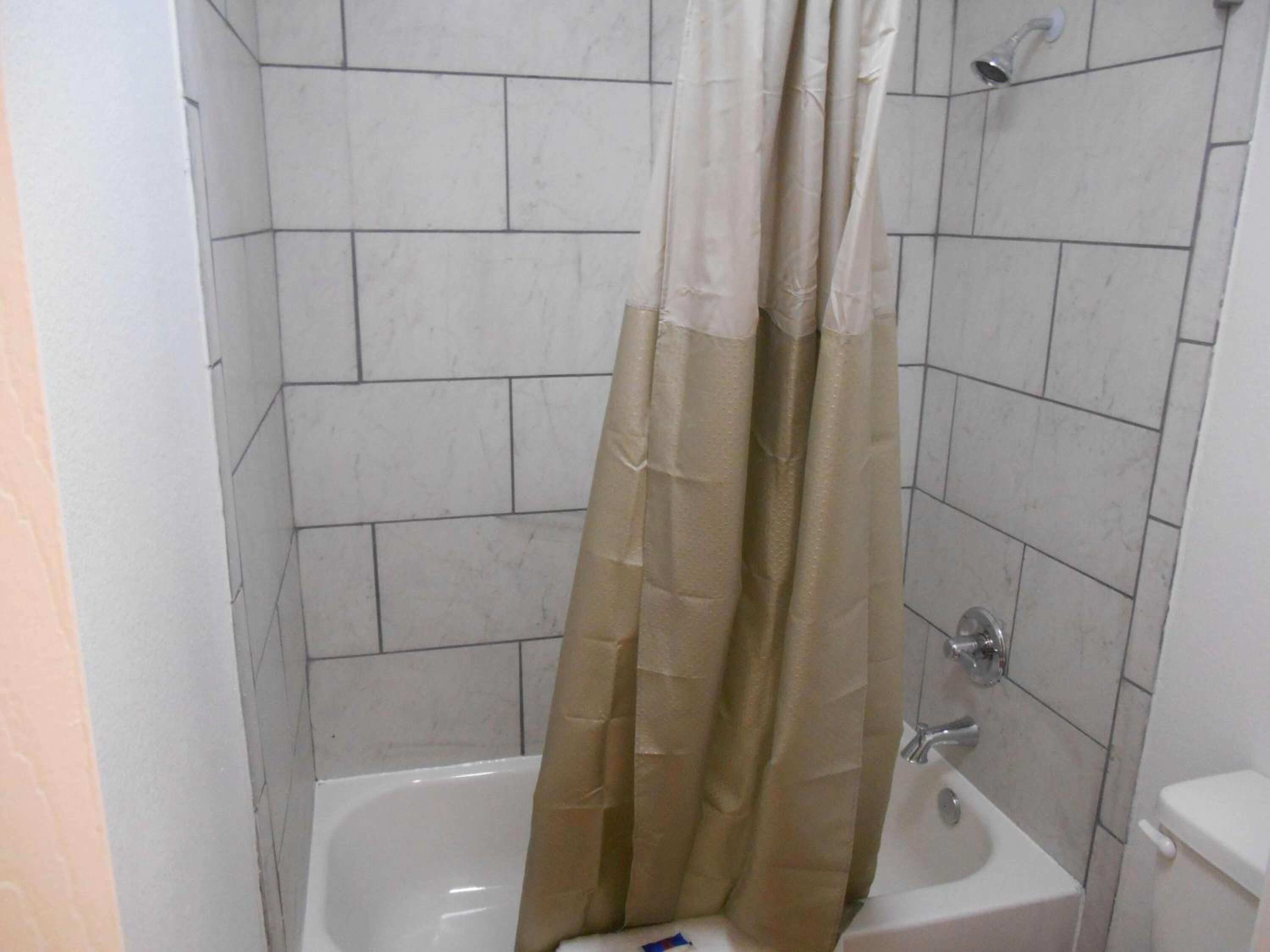 A small, tiled bathroom with a bathtub, a toilet, and a shower curtain.