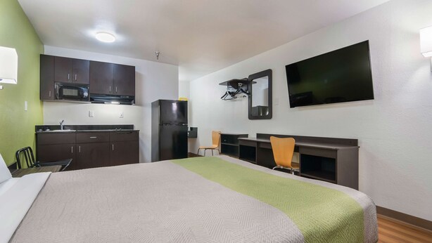 Habitación de hotel con cama, kitchenette, televisión y espejo.