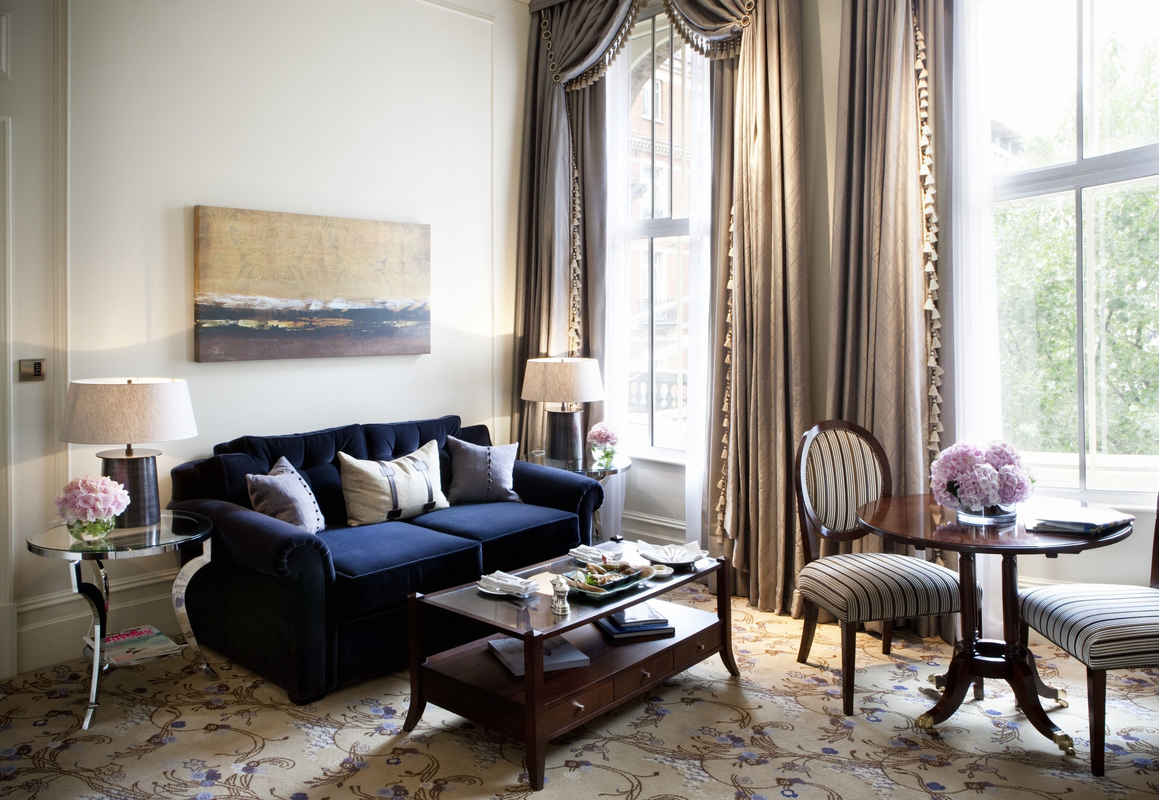 A living room with a blue sofa, a coffee table, a striped chair, a small table with flowers, and a painting on the wall.