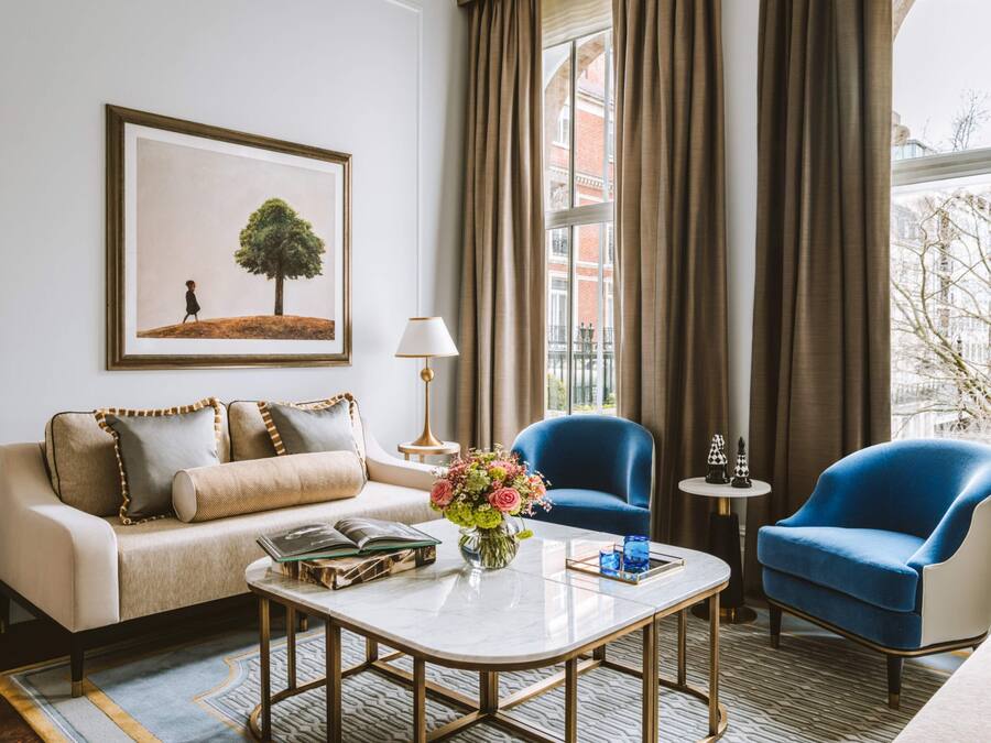 A modern hotel room with a sofa, two armchairs, a coffee table, and a framed picture on the wall.