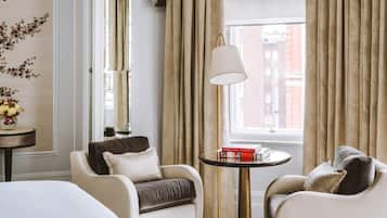 A hotel room with two armchairs, a small round table with books, a lamp, and a window with curtains.