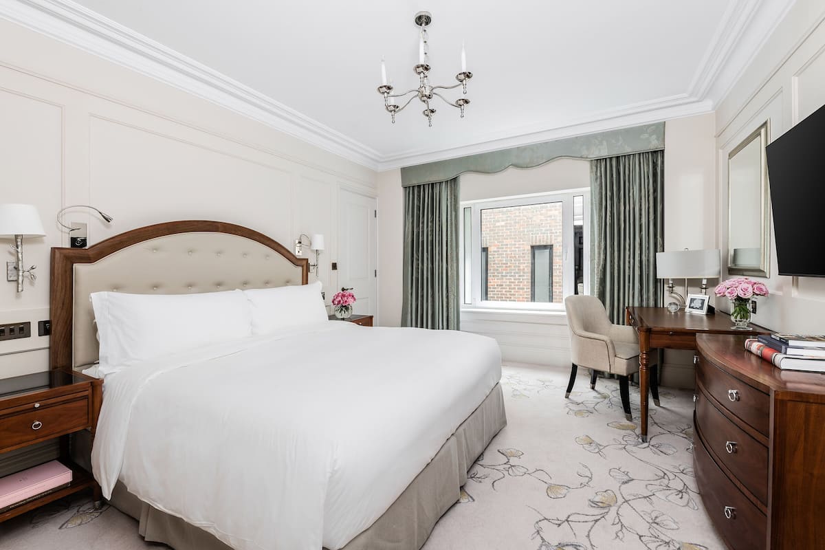 A hotel room with a large bed, a desk, a chair, a dresser, and a television.