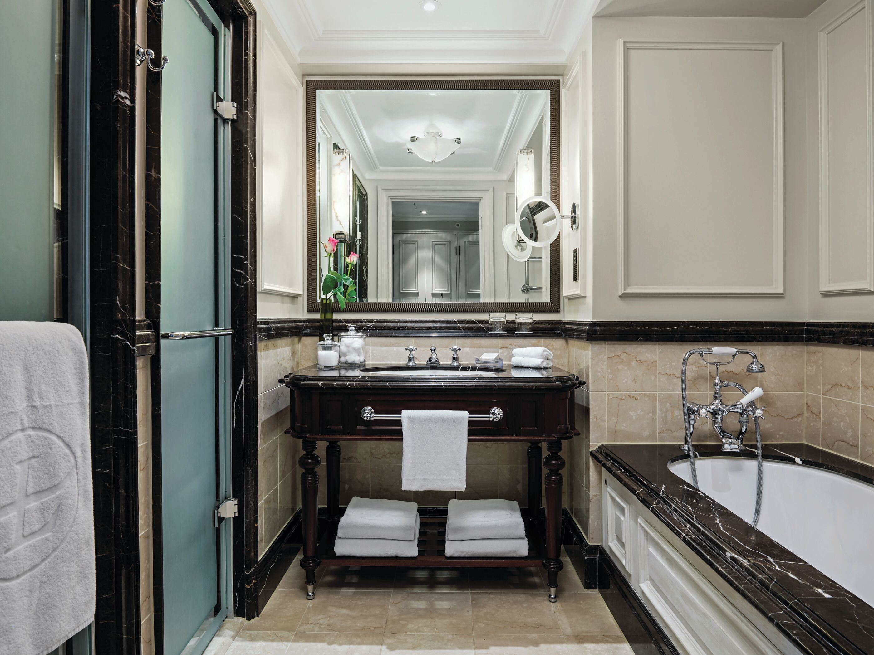 Une salle de bain luxueuse avec un meuble-lavabo en marbre, un grand miroir, une baignoire et un porte-serviettes.
