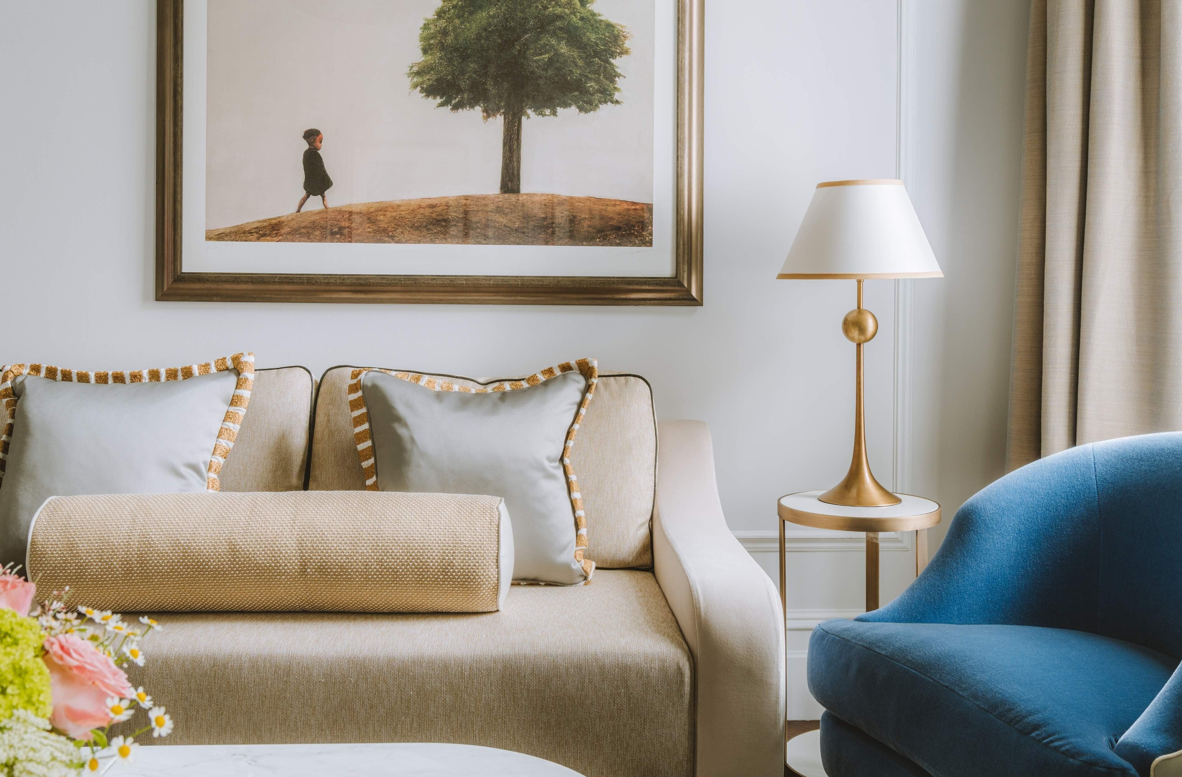 Una sala de estar con un sofá color beige, un sillón azul, un cuadro en la pared y una lámpara de pie.