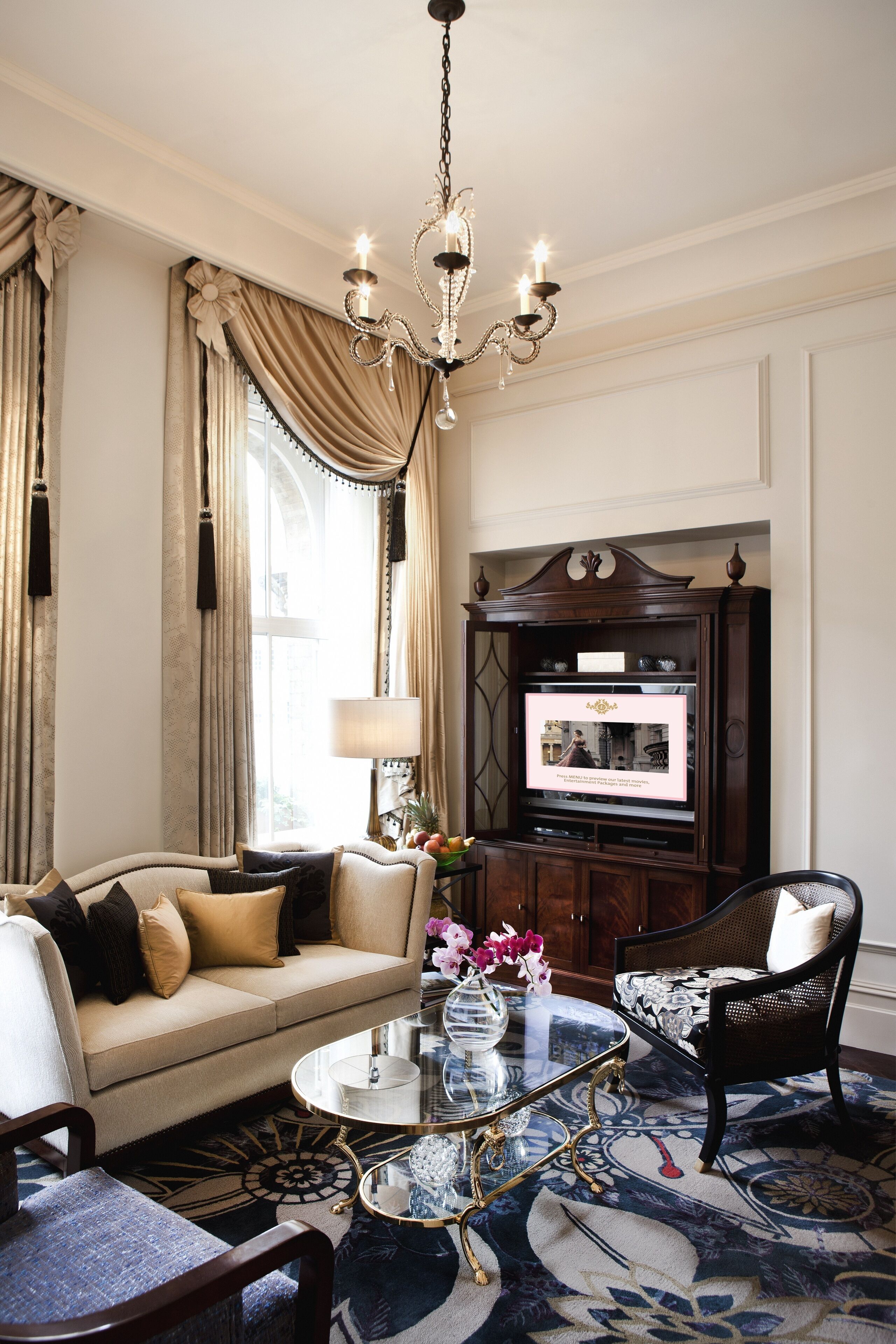 A living room with a sofa, armchairs, a coffee table, a chandelier, and a television on a wooden cabinet.