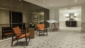A room with a patterned carpet, wooden chairs, a small table, a mirror, and a cabinet with decorative items.