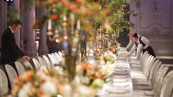 Una larga mesa de banquete con centros de flores y candelabros, ubicada en un comedor formal con sillas elegantes.