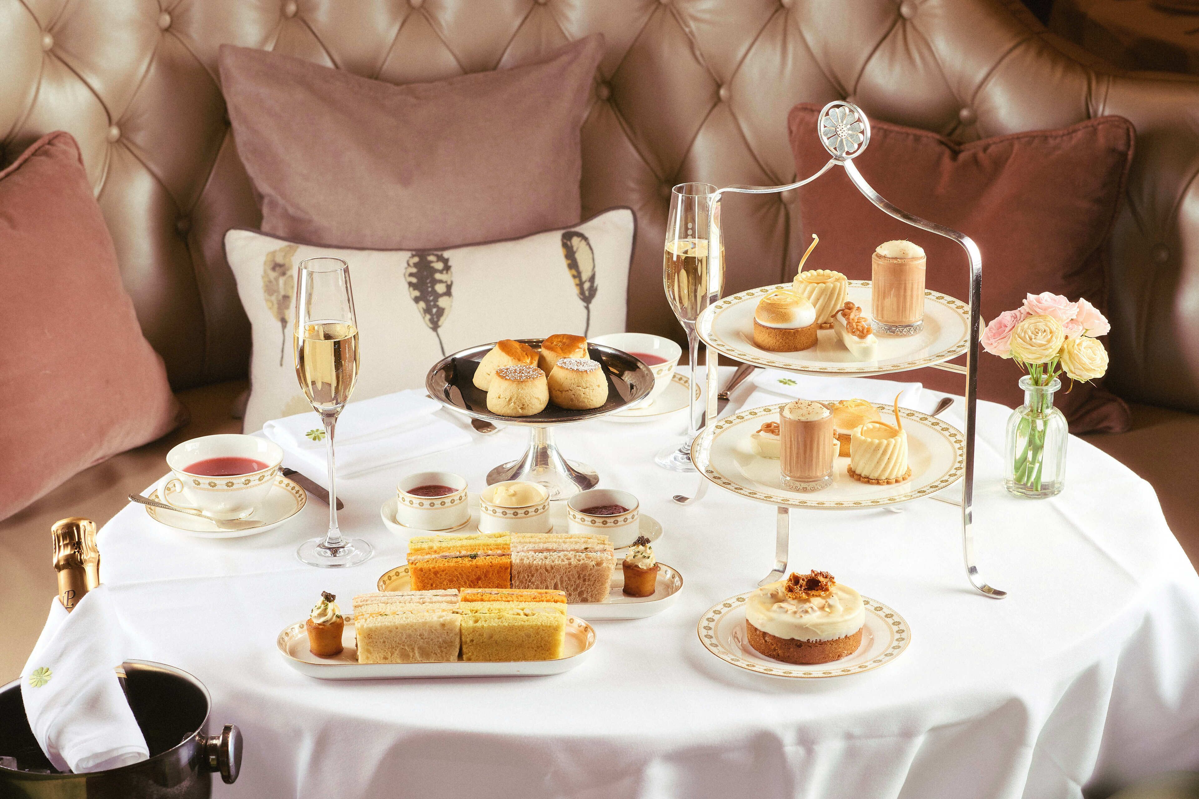 A table set with a variety of pastries and desserts, a glass of champagne, and a tea service.