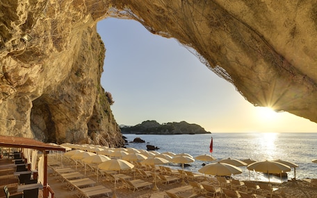 A beach with sun umbrellas and lounge chairs under a large rock formation.