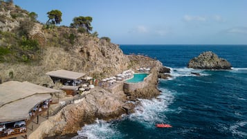 A coastal hotel with a pool, outdoor seating, and a rocky cliff backdrop.