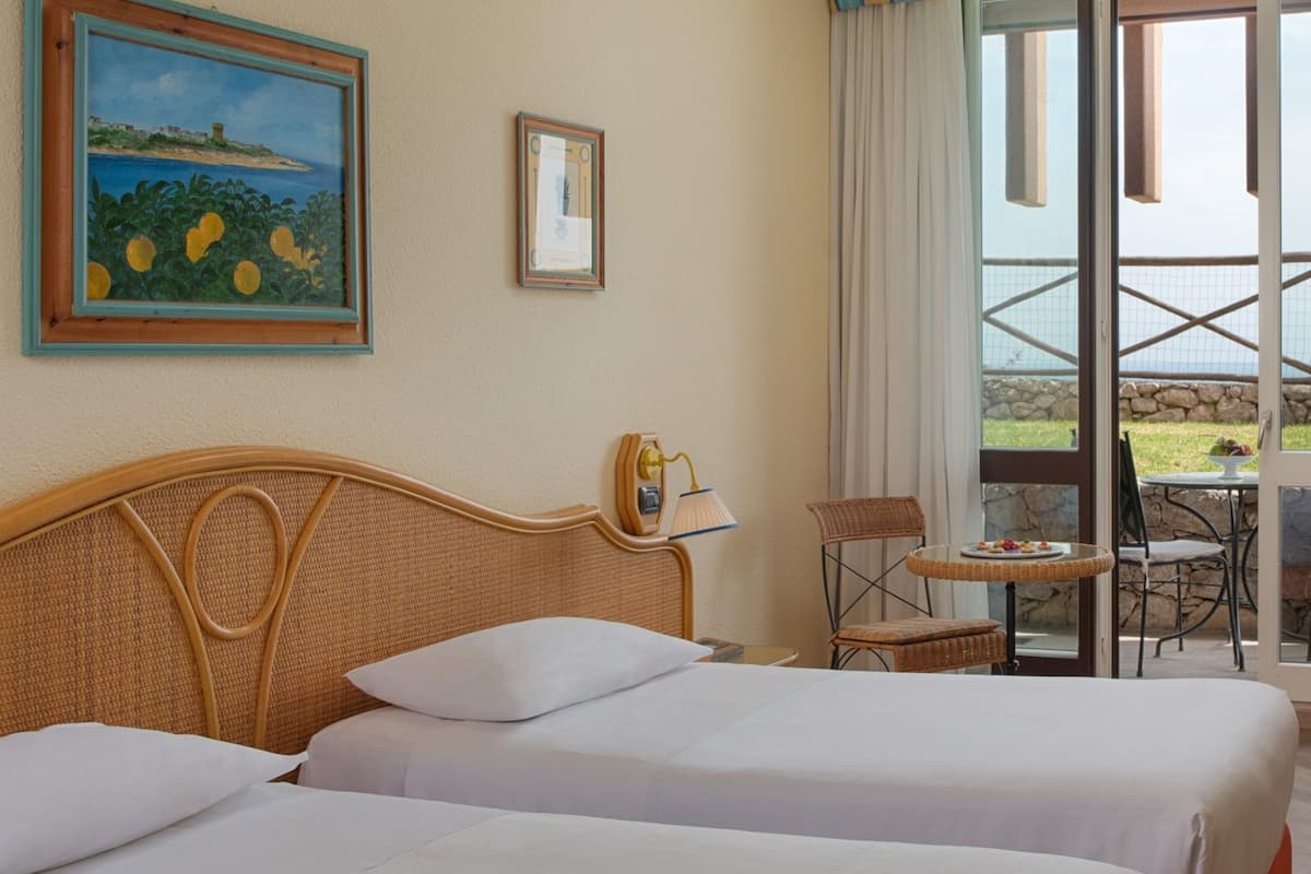 Habitación de hotel con dos camas, un cuadro, un certificado enmarcado, una lámpara, una mesa con una bandeja de fruta y vistas al exterior.
