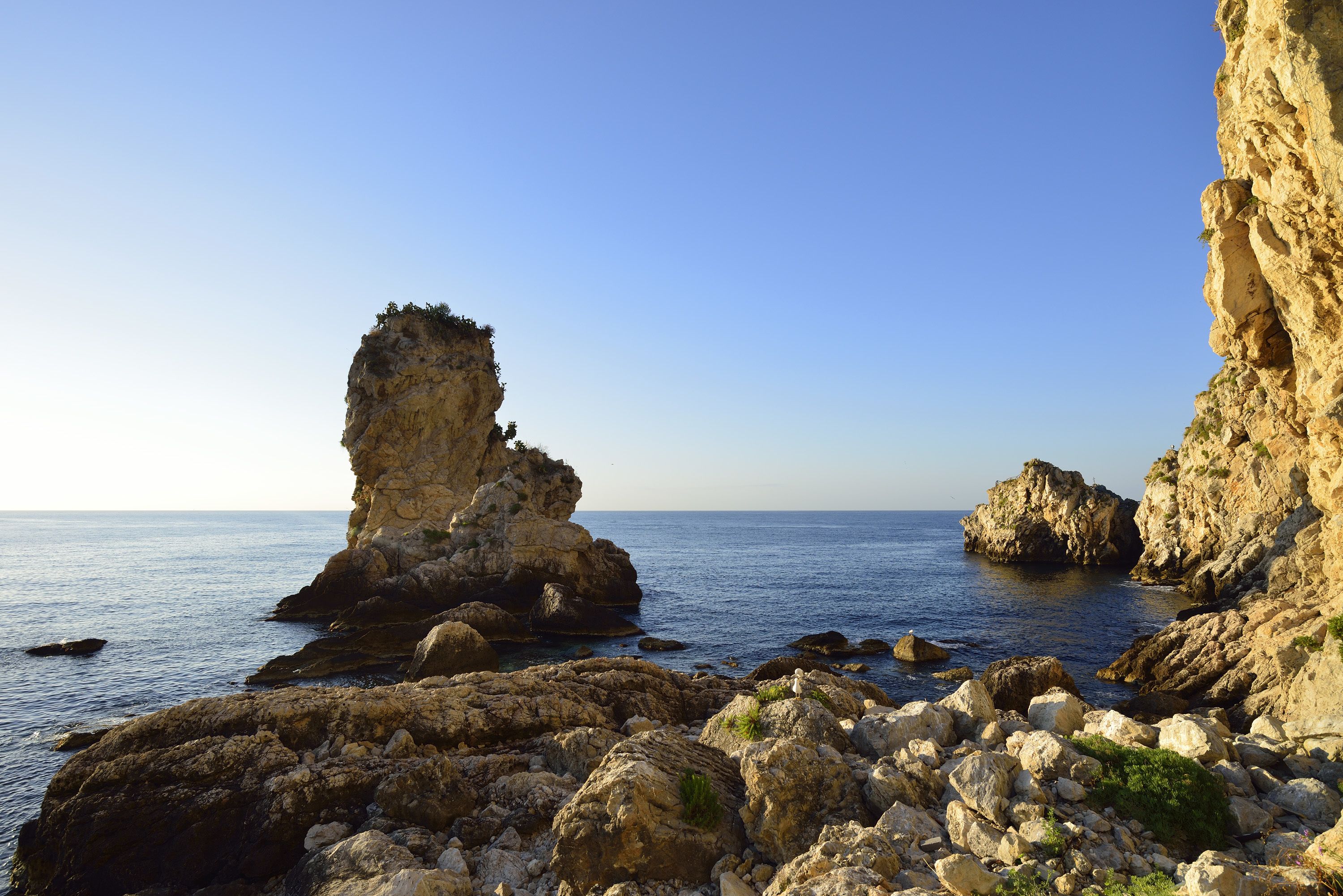 A rocky coastal landscape with prominent rock formations and clear blue sea.