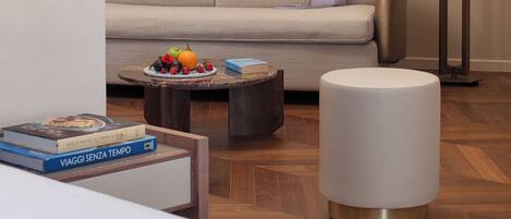 A modern living room with a sofa, a round coffee table with fruits, a lamp, and a bookshelf with books.