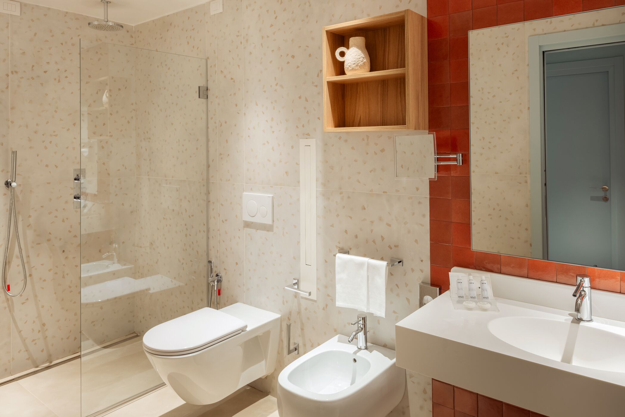 A modern bathroom with a glass-enclosed shower, a white toilet, a bidet, and a double sink with a mirror above.