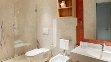 A modern bathroom with a glass-enclosed shower, a white toilet, a bidet, and a double sink with a mirror above.
