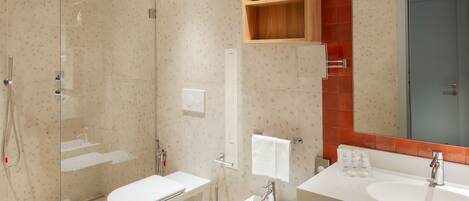 A modern bathroom with a glass-enclosed shower, a white toilet, a bidet, and a double sink with a mirror above.