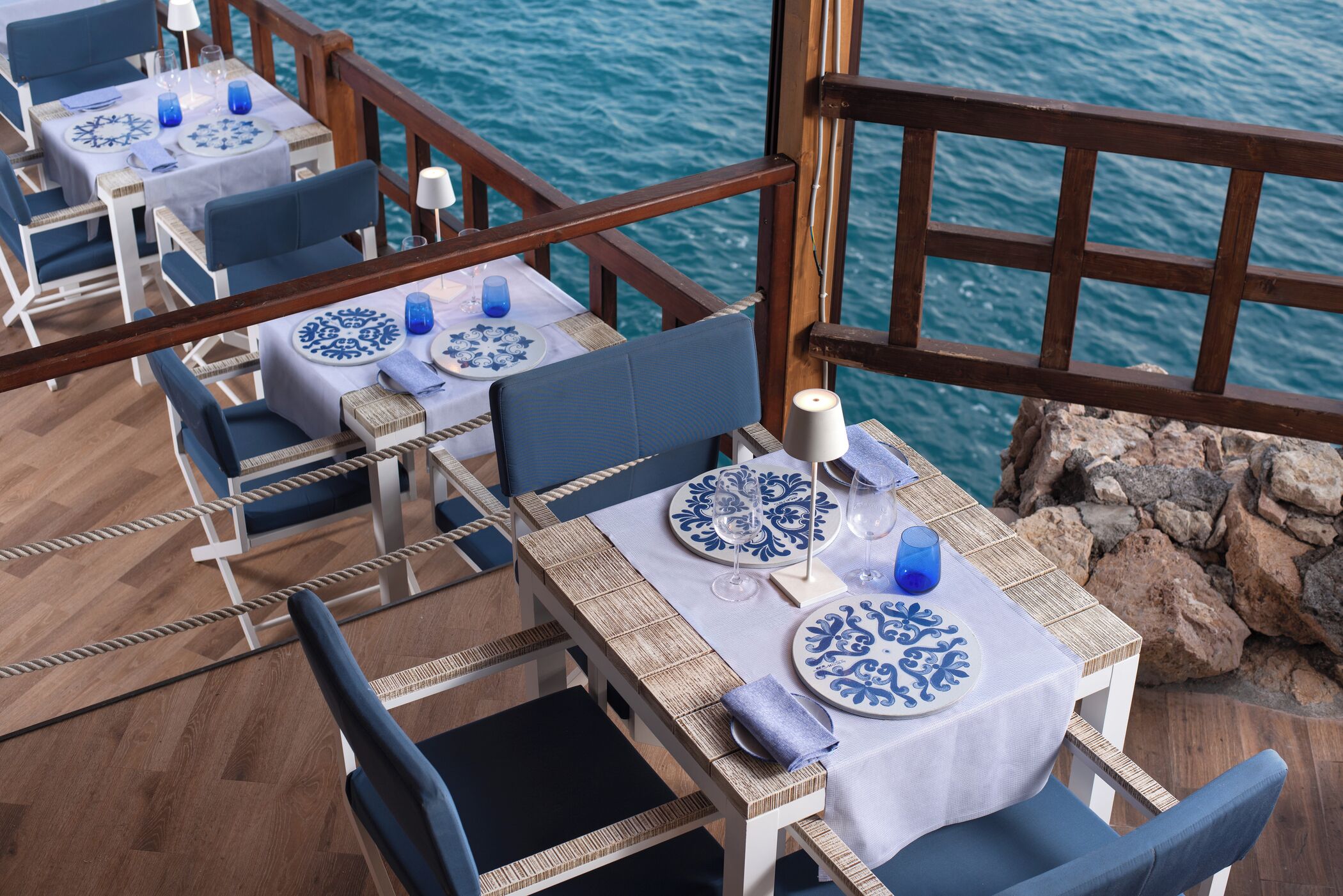 Un espace repas avec des tables préparées pour deux personnes, donnant sur un plan d’eau.