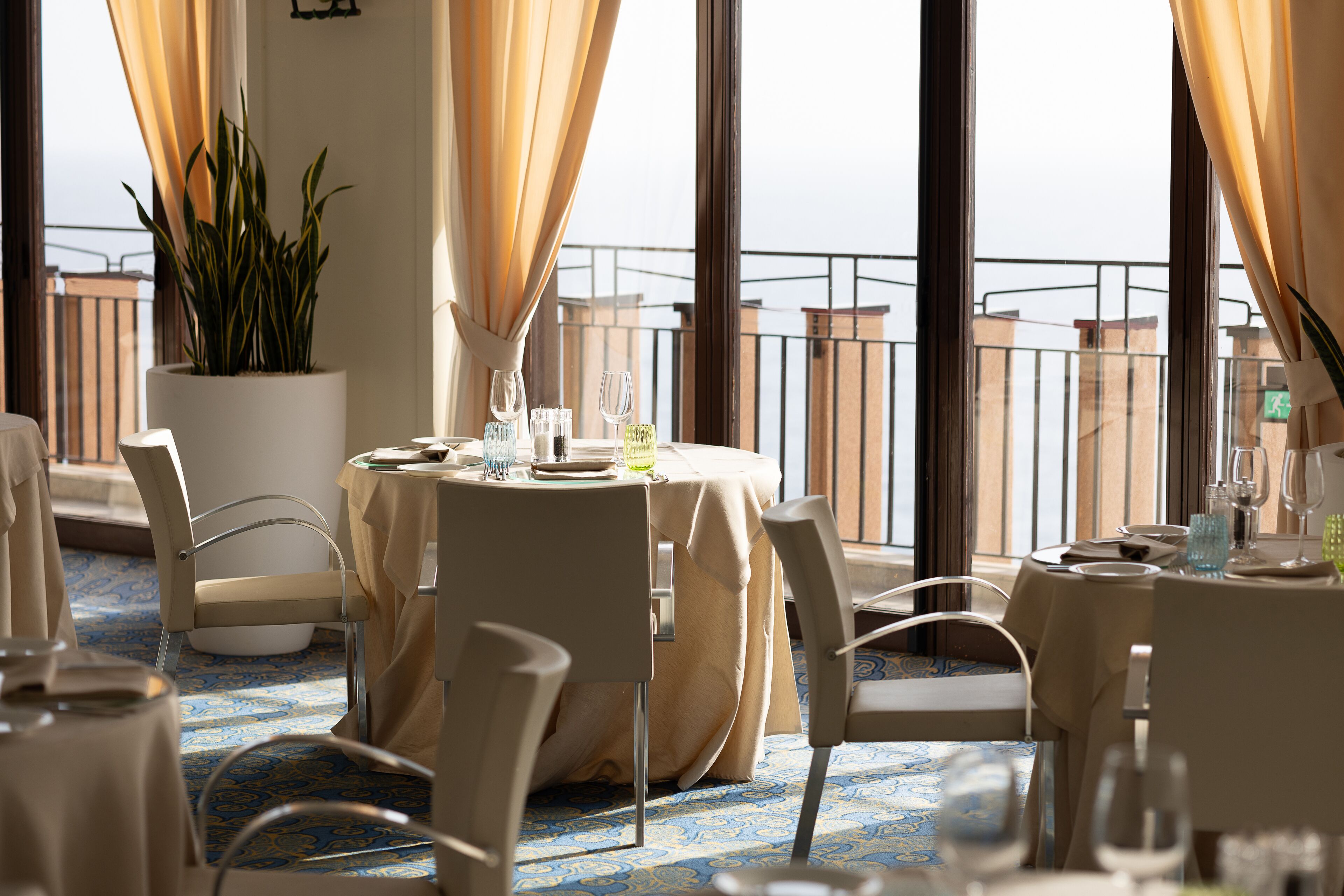 Un comedor con una mesa para dos personas, una planta en maceta y vistas de la ciudad a través de amplios ventanales.