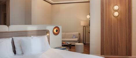A hotel room with a large bed, a sofa, a small table with a lamp, and a wooden wardrobe.