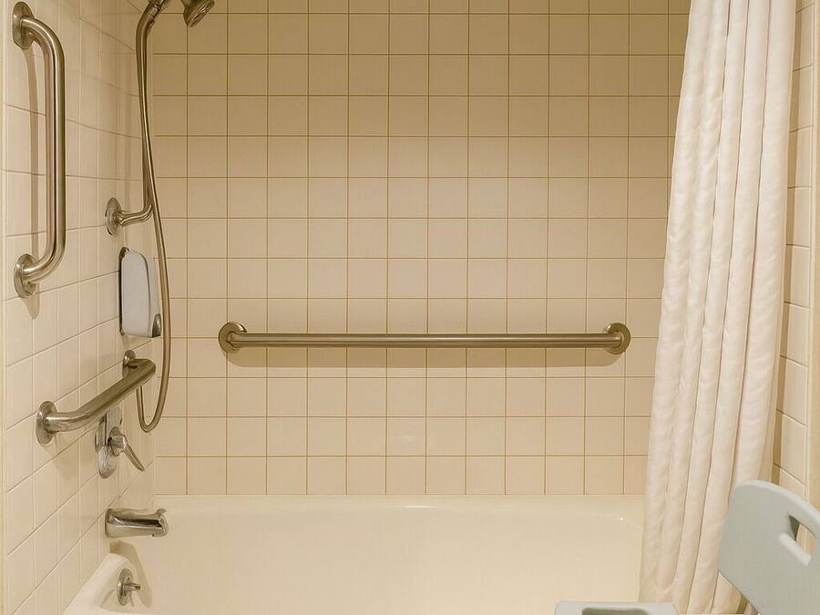 Ein Badezimmer mit Badewanne, Haltegriffen, Duschkopf und einer rollstuhlgerechten Sitzbank.
