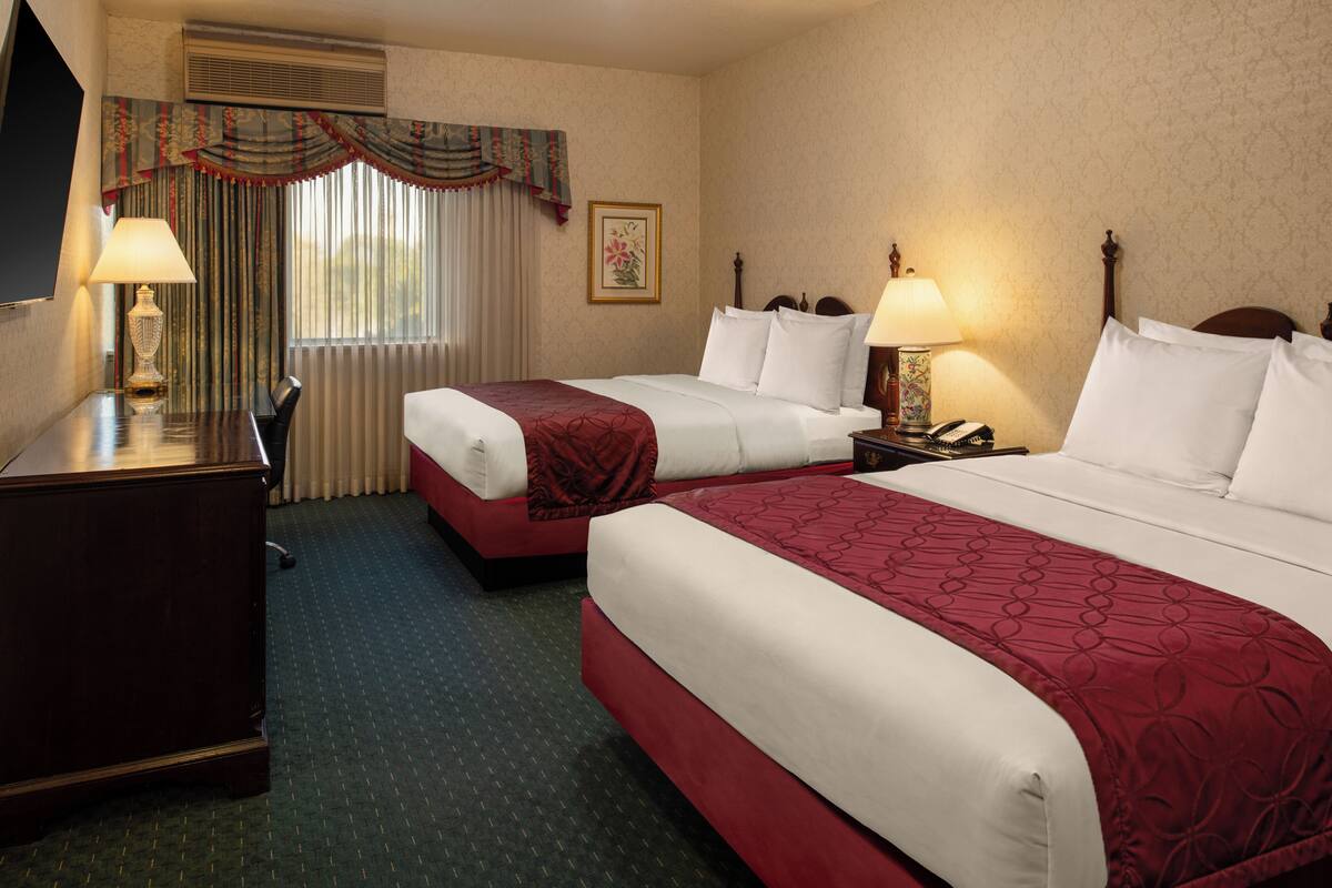 A hotel room with two beds, a desk, a chair, and a television.