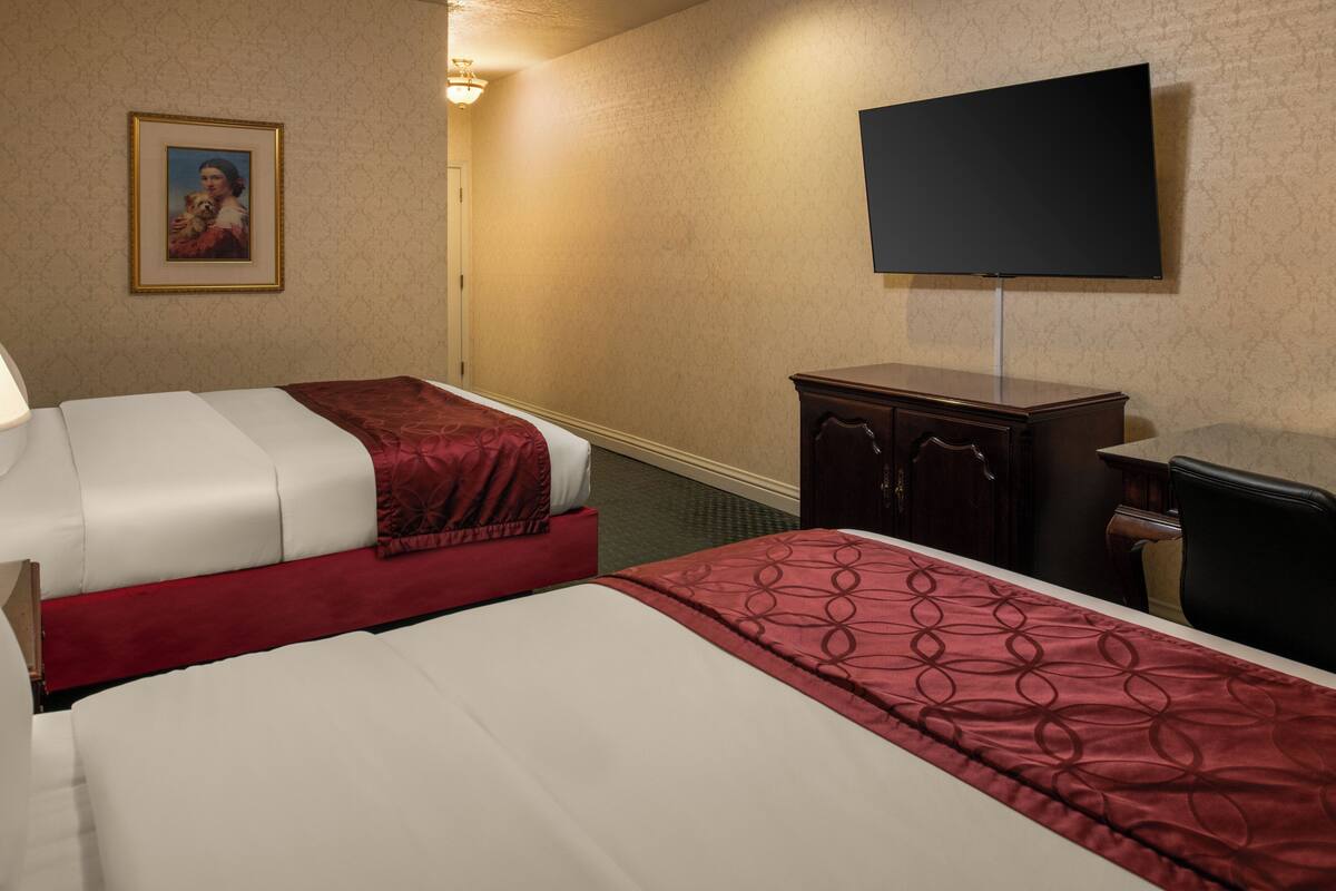 A hotel room with two beds, a TV, a cabinet, and a framed picture on the wall.