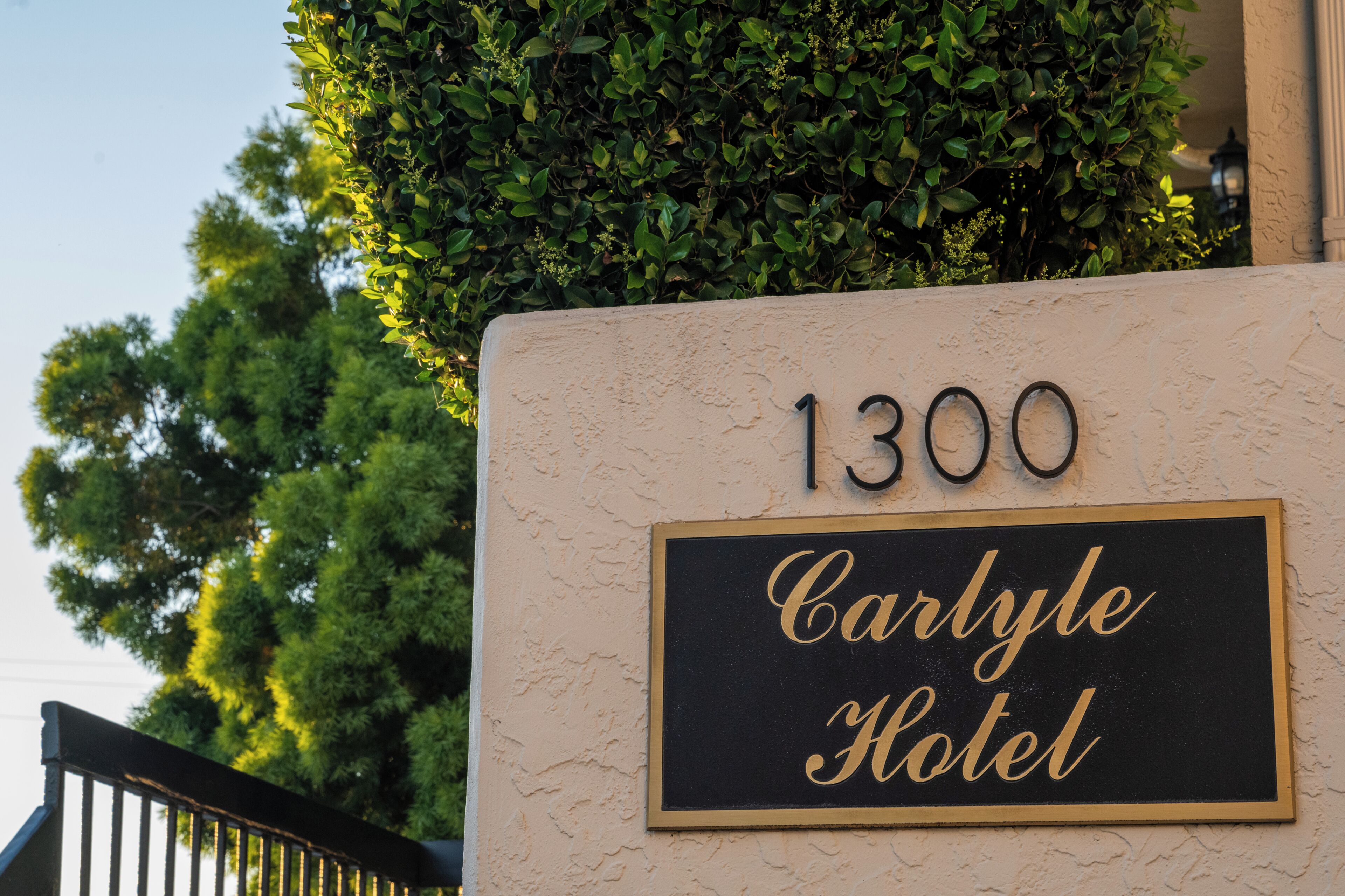 A sign for the Carlyle Hotel with the number 1300, surrounded by greenery.
