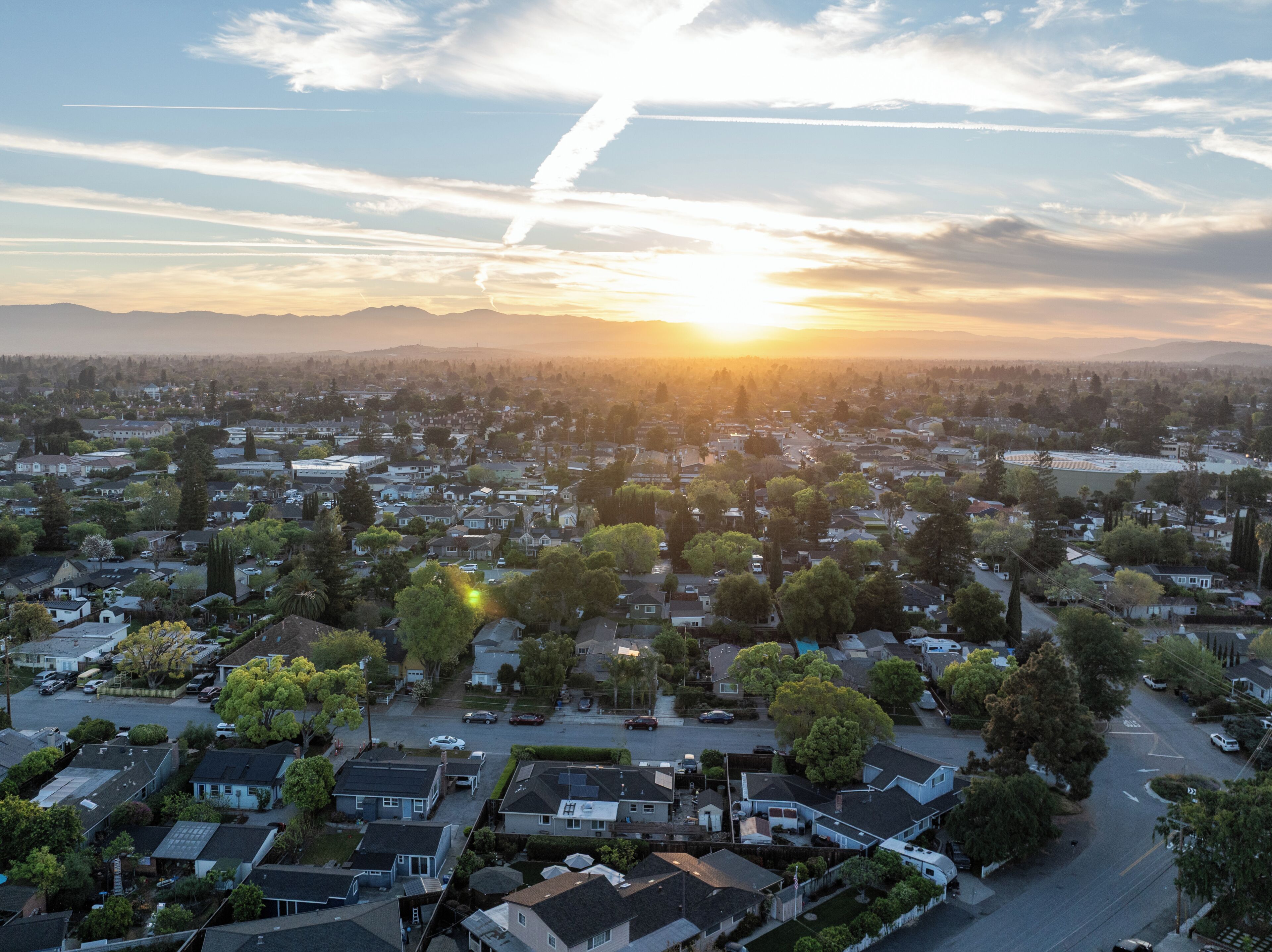 An aerial view of a residential area with houses, streets, and a sunset in the background.