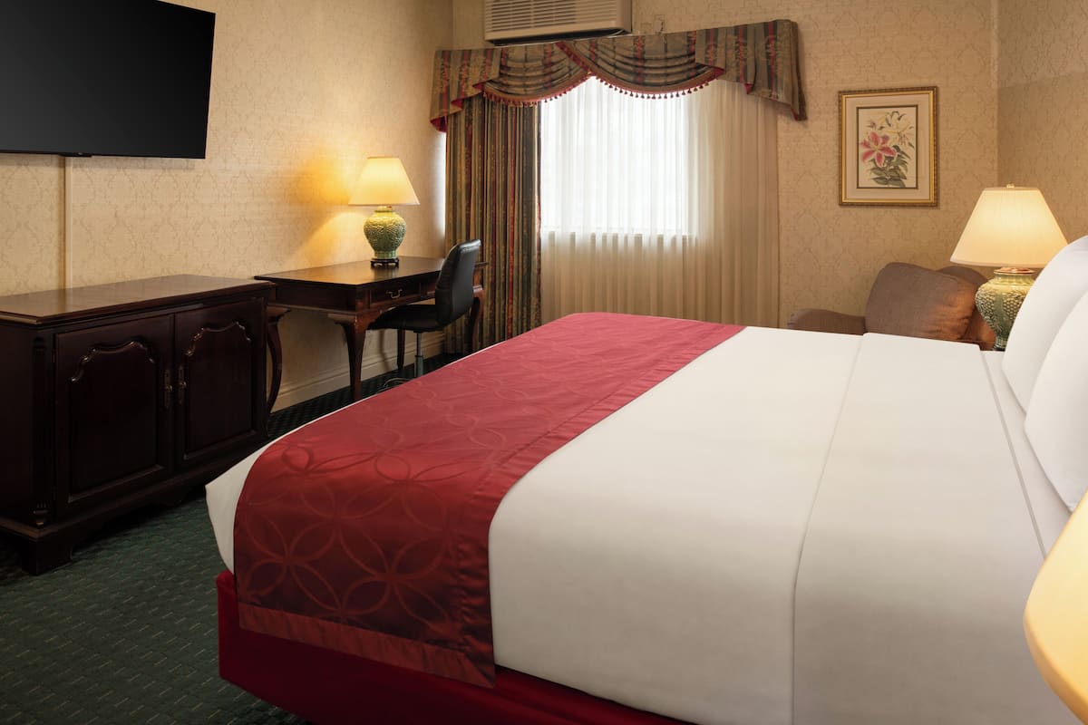 A hotel room with a bed, desk, chair, lamps, and a television.