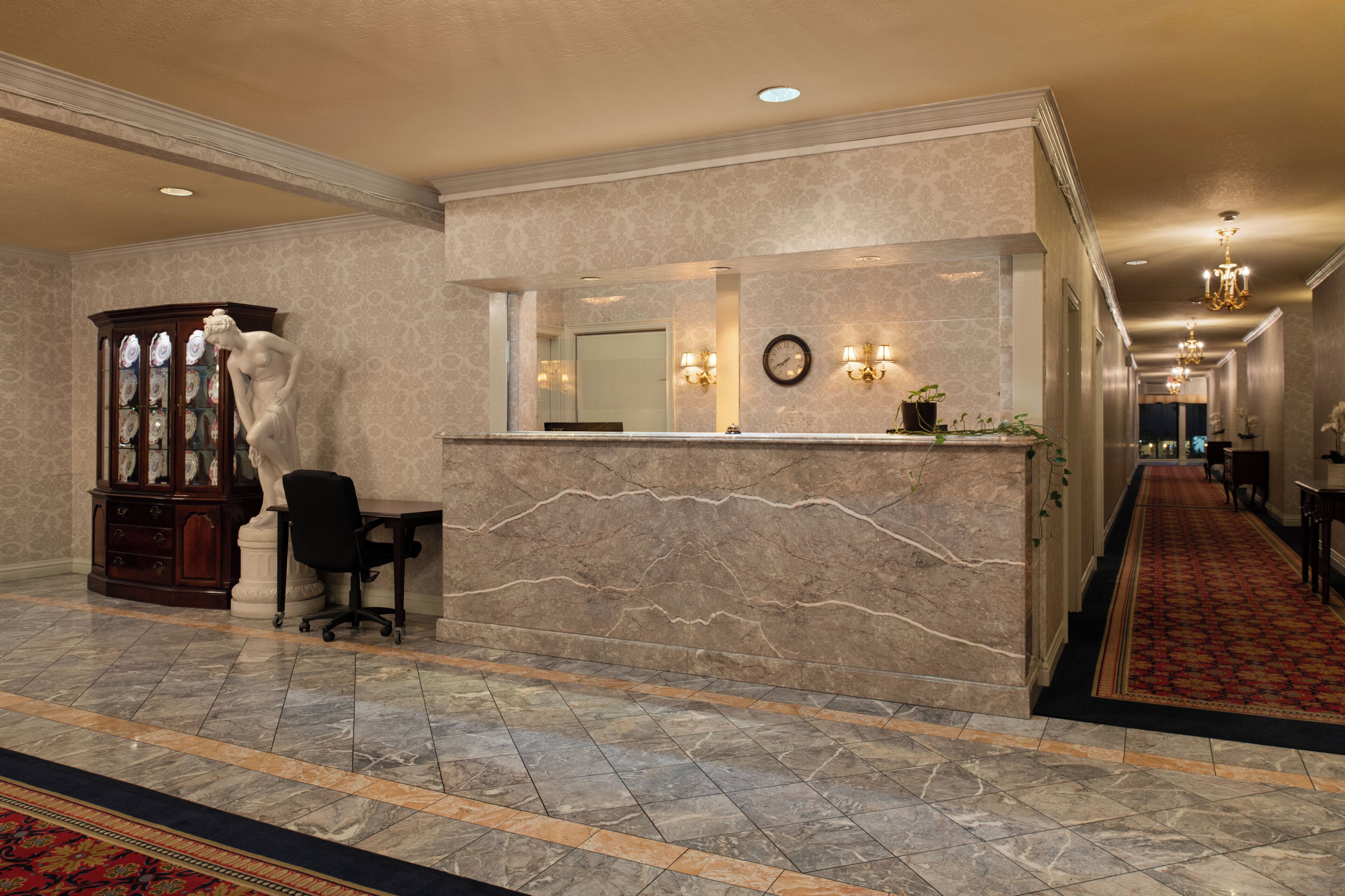 A reception area with a marble counter, a statue, a desk, and a patterned carpet.