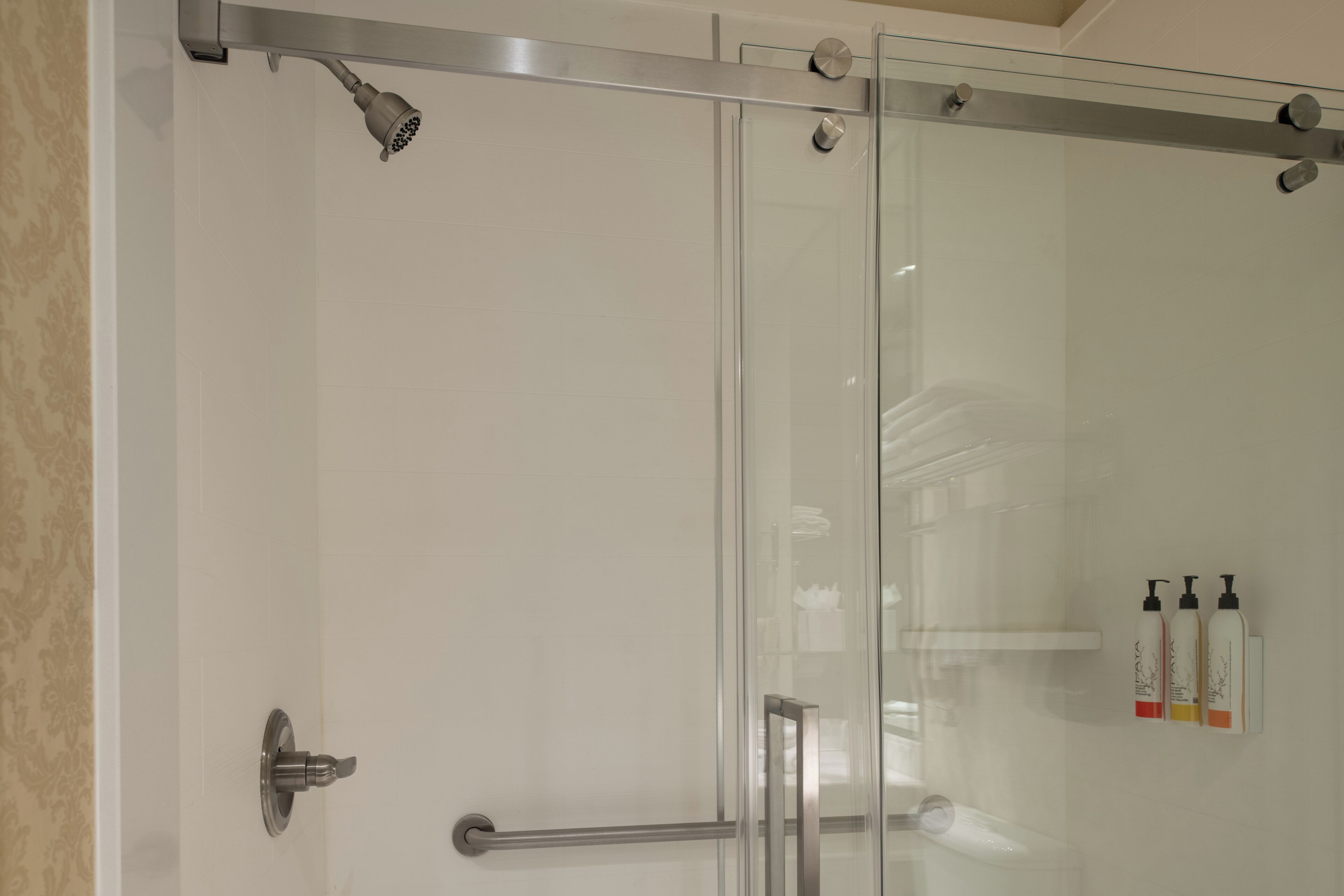 A glass-enclosed shower with a handheld showerhead and a control panel.