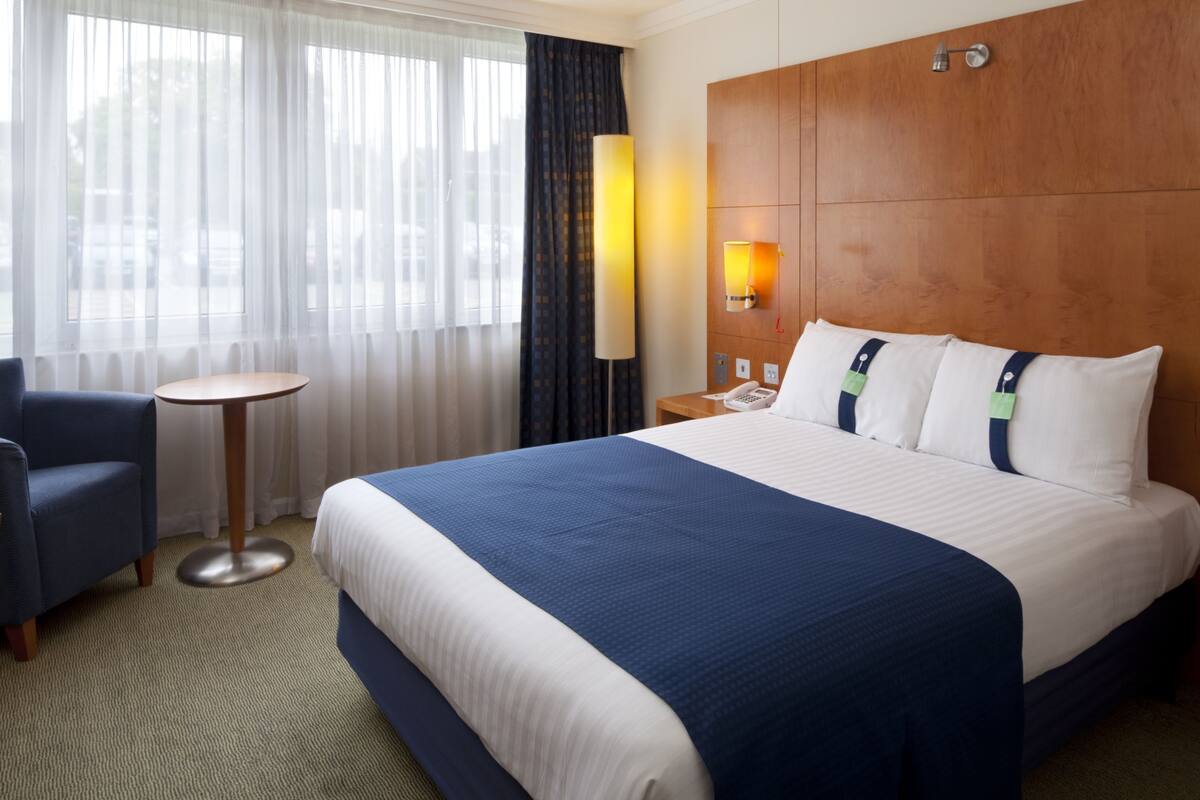 Une chambre d’hôtel avec un grand lit, un bureau, une chaise et une fenêtre avec des rideaux.
