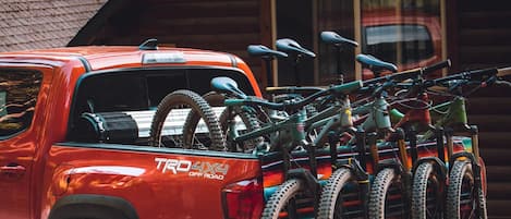 A red pickup truck with a bike rack loaded with bicycles parked in front of a wooden cabin.