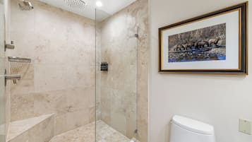 A modern bathroom with a glass-enclosed shower, a white toilet, and a framed picture of bears on a river.