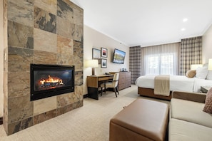 A modern hotel room with a fireplace, a bed, a desk, and a couch.