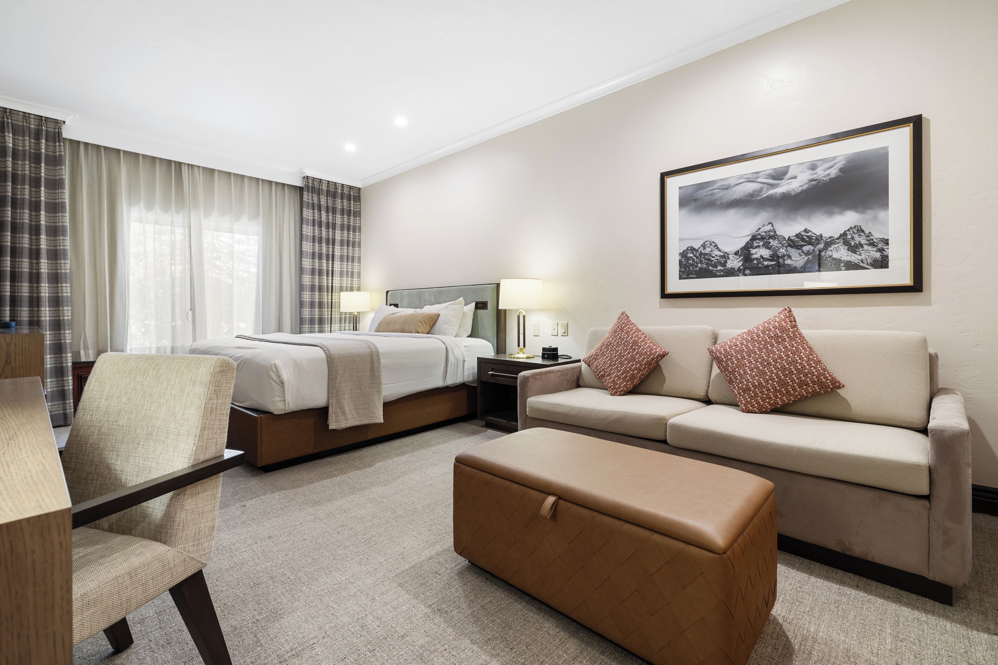 A hotel room with a bed, a sofa, a chair, a table, and a large framed picture on the wall.