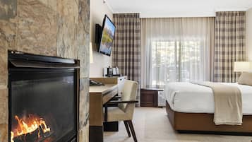 A hotel room with a fireplace, a bed, a desk with a chair, and a television mounted on the wall.