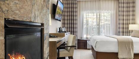 Habitación de hotel con chimenea, cama, escritorio con silla y televisor montado en la pared.