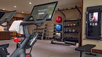 A home gym with exercise equipment, a treadmill, a stationary bike, and a wall-mounted screen displaying workout instructions.