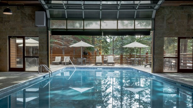 Une piscine à l’eau claire, entourée de chaises longues et de parasols, avec vue sur les arbres et une terrasse en bois.