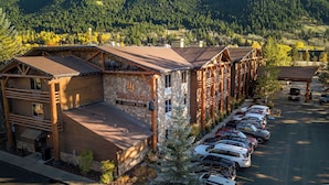 Un chalet à l’aspect rustique, avec une façade en bois, une enseigne indiquant « The Lodge at Jackson Hole », et un parking où sont garées plusieurs voitures.