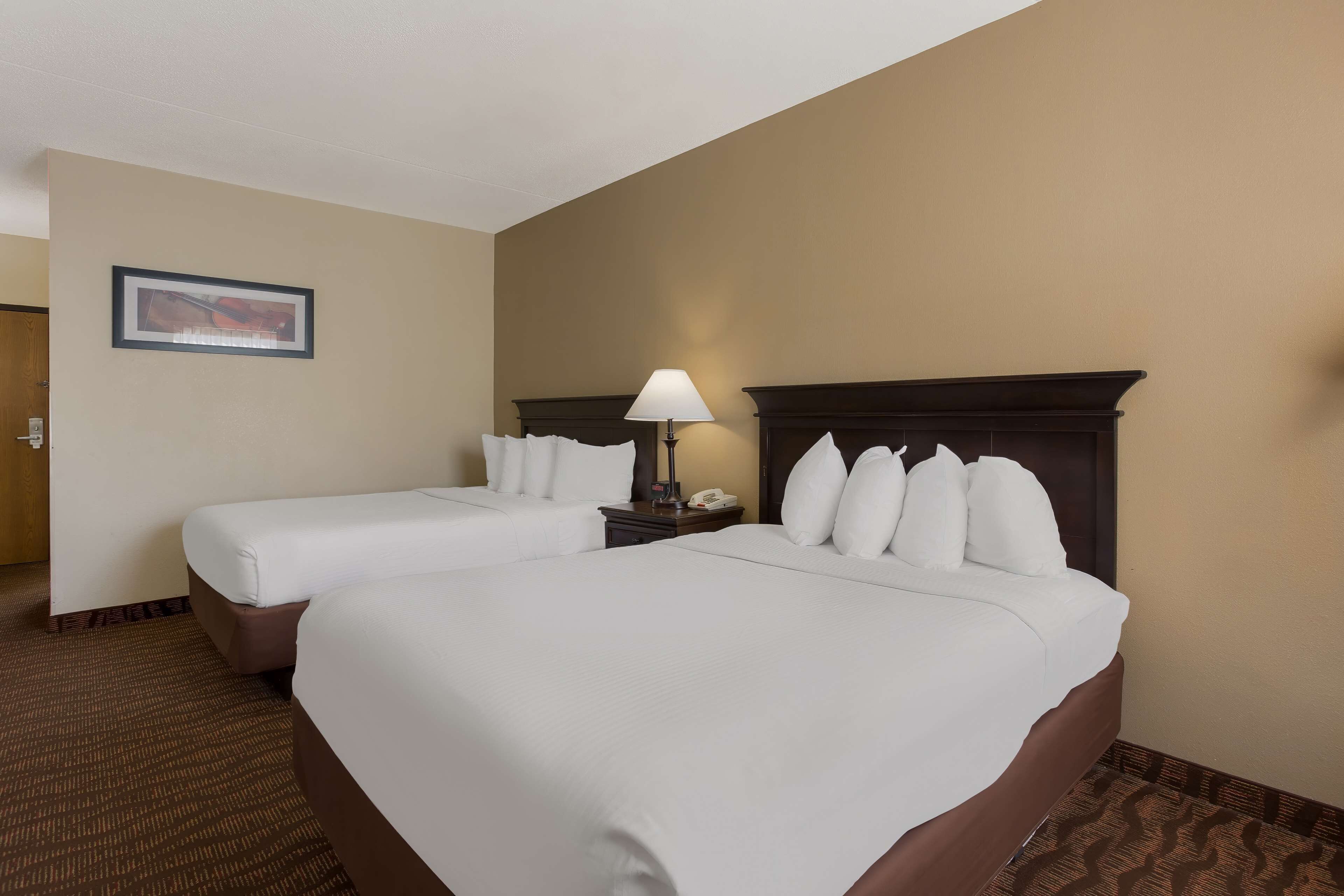 A hotel room with two beds, a nightstand with a lamp, and a framed picture on the wall.