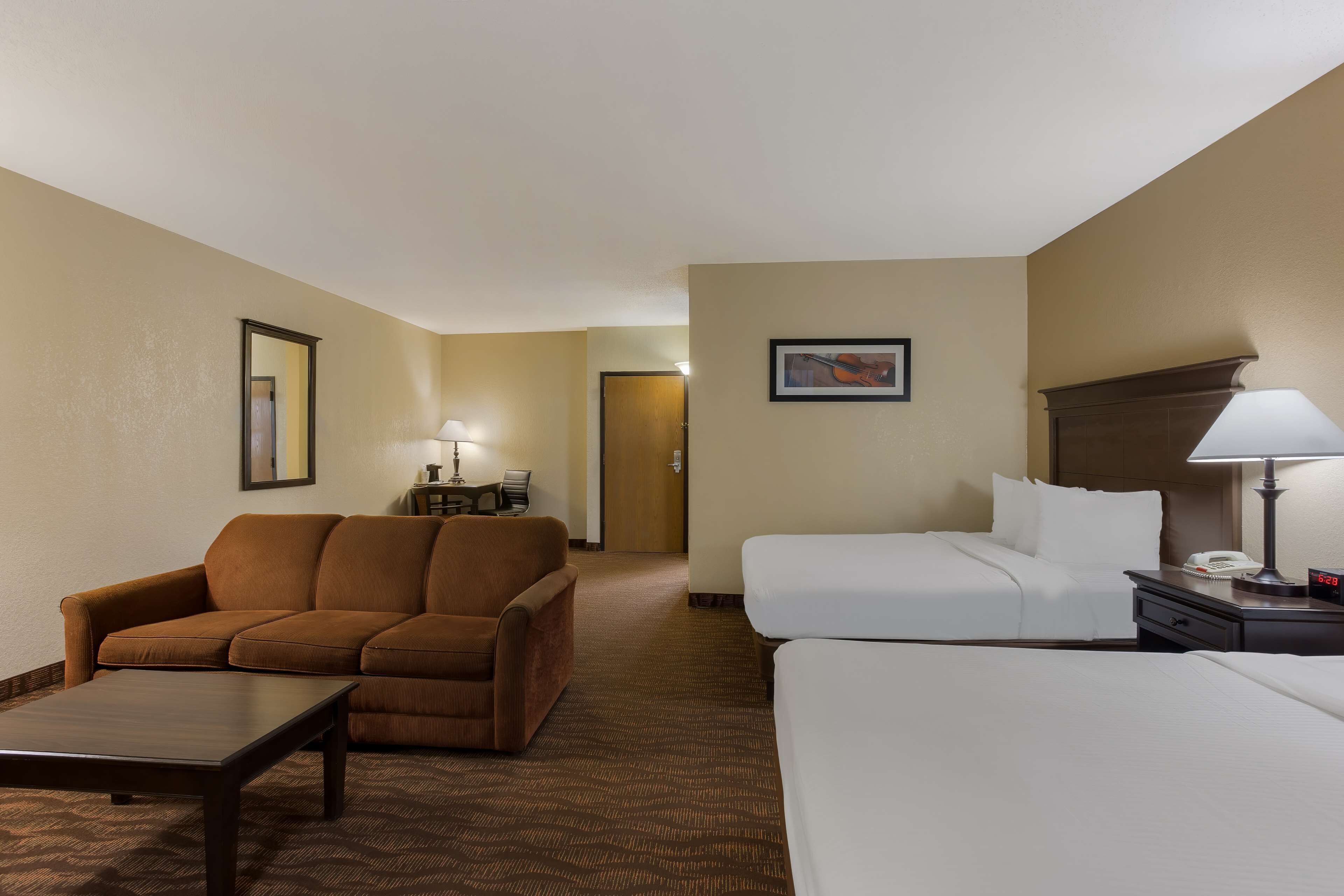 A hotel room with a sofa, a bed, a nightstand with a lamp, and a framed picture on the wall.