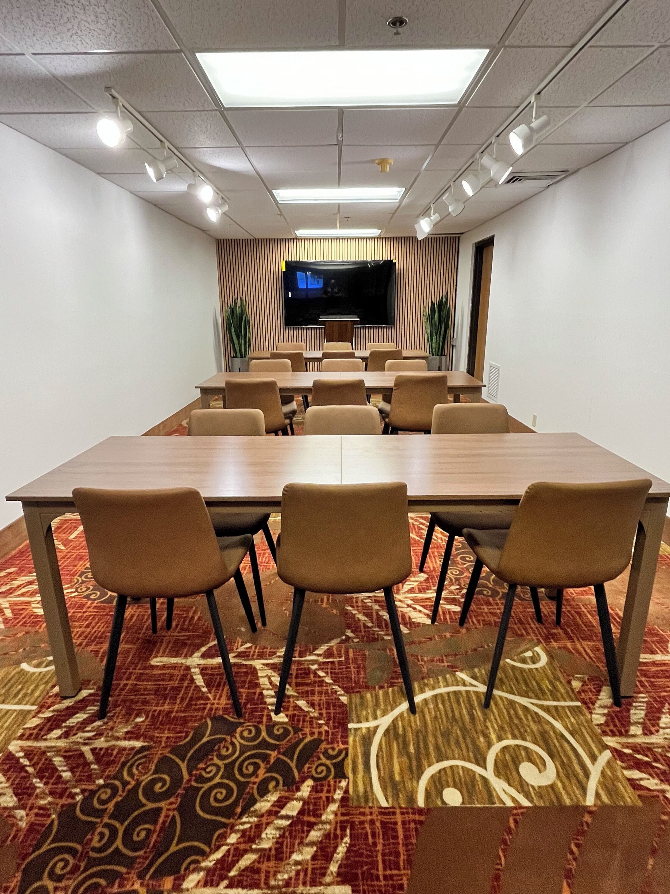 A conference room with a long table, chairs, a flat-screen TV, and patterned carpet.