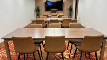 A conference room with a long table, chairs, a flat-screen TV, and patterned carpet.