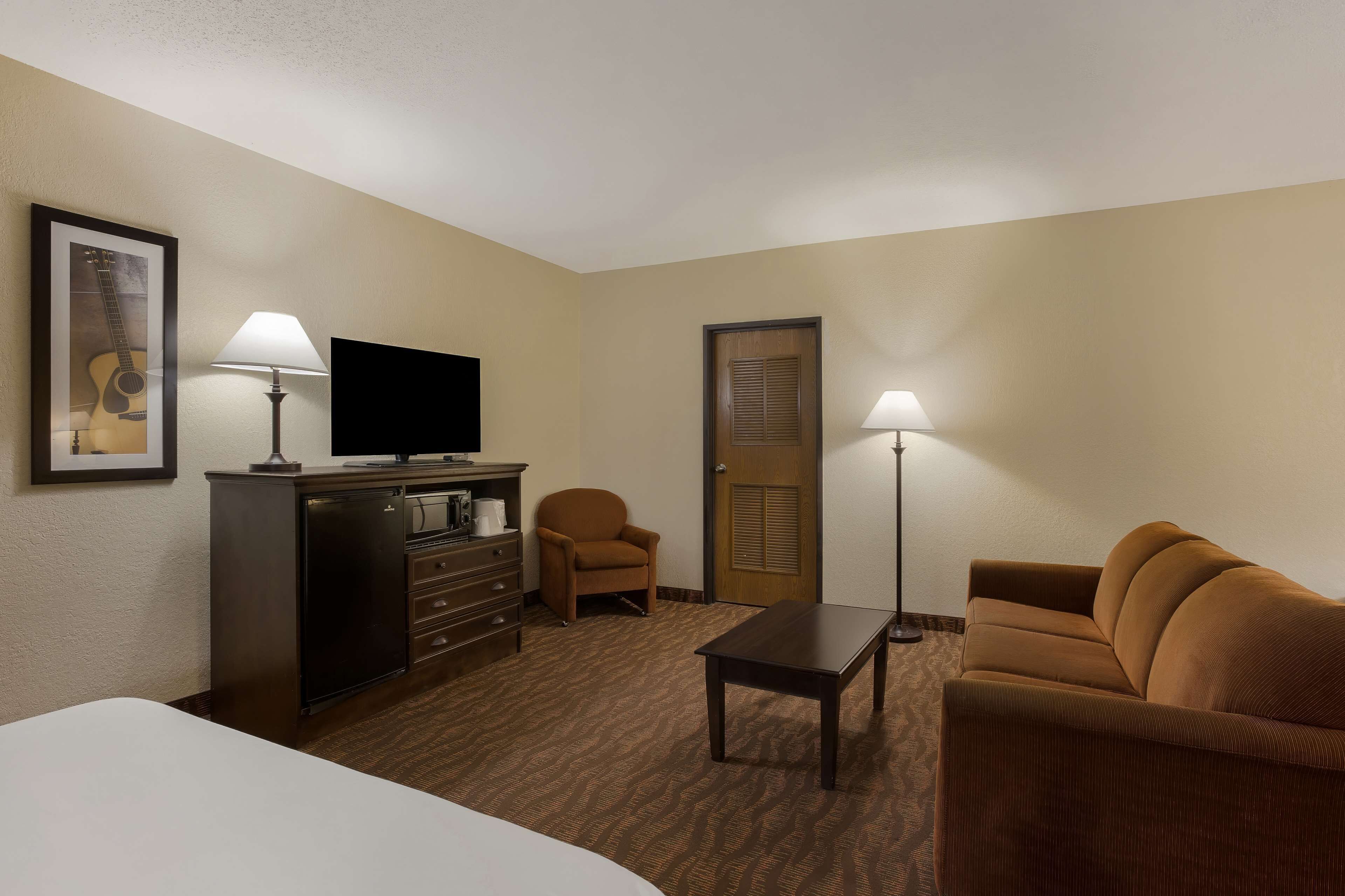A hotel room with a bed, a desk, a television, a chair, a sofa, and a lamp.